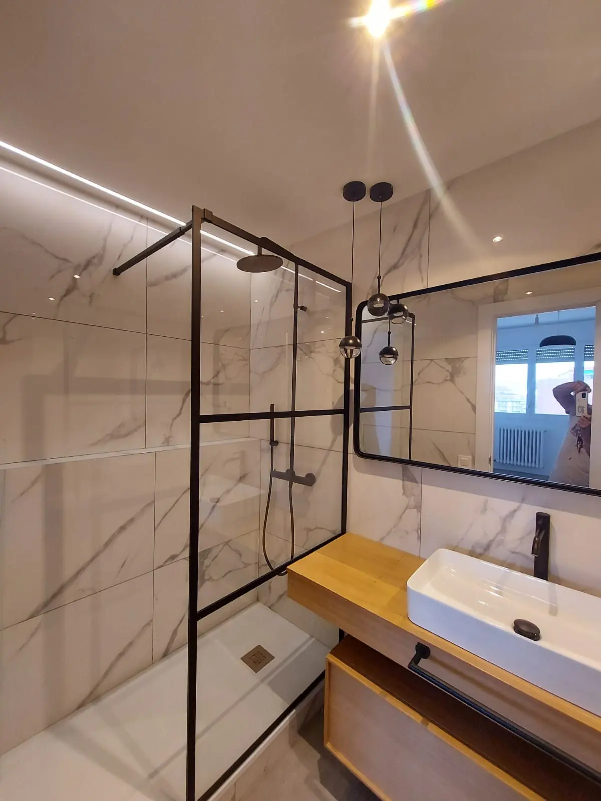 Baño reformado con mampara de perfil negro, revestimiento efecto mármol y mueble de madera
