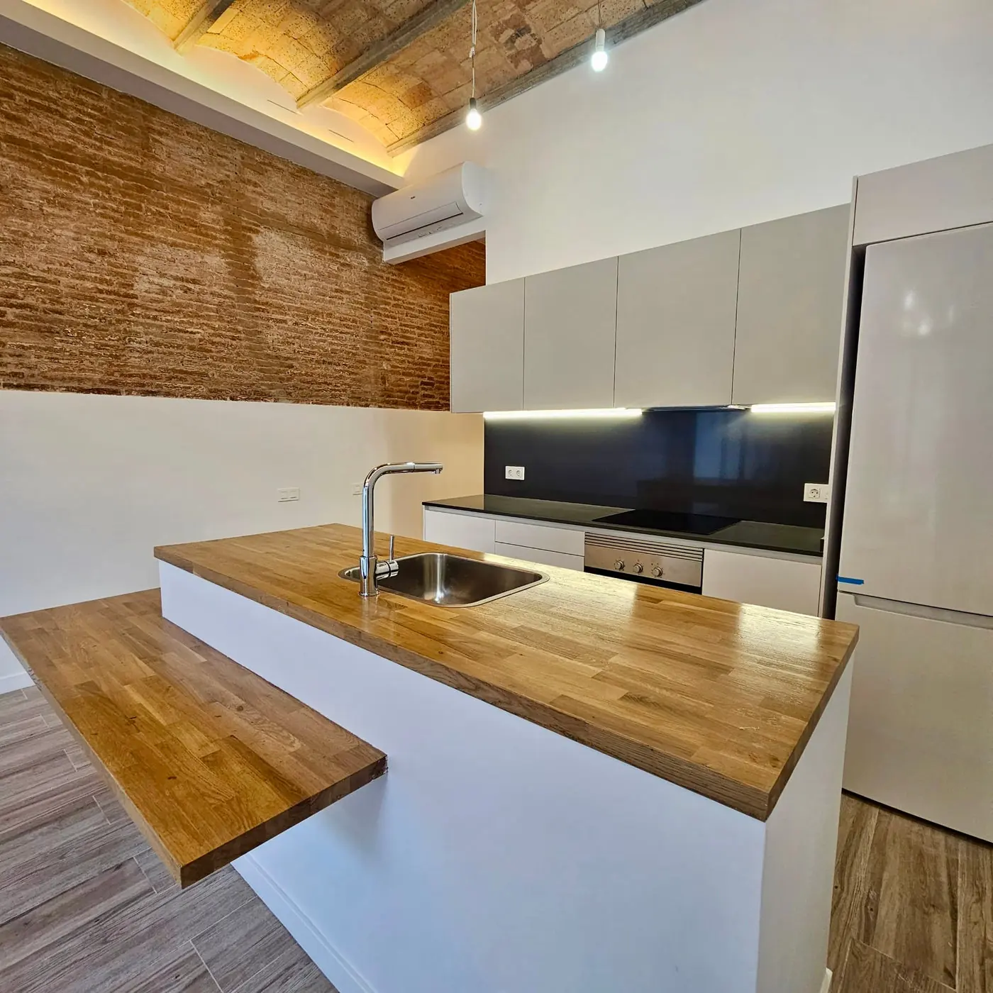 Cocina reformada con encimera de madera y pared de ladrillo visto